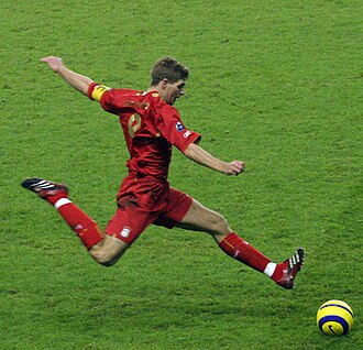 Gerrard wearing an all-red kit and kicking a yellow ball in a match