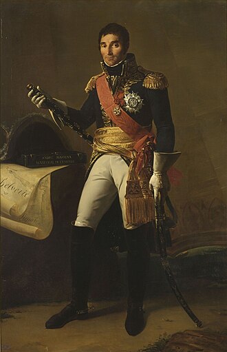 Formal full-length portrait of Masséna in dress military uniform, comprising white breeches with knee length black boots, dark cutaway coat with high collar and gold embroidery, a red shoulder sash and gold waist sash. He wears a large star of honour on his breast. He is a tall dark man with a long face and thick eyebrows. He looks quizzically at the observer and holds a marshal’s baton, and sabre.