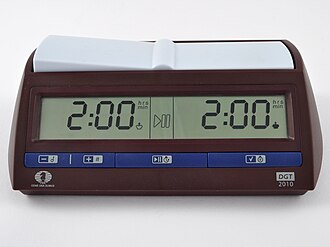 A brown chess clock with blue buttons along the bottom. A digital display shows the time remaining for each side