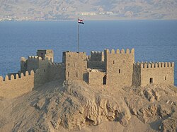 Orqa fonda dengiz va Misr bayrogʻi koʻrinib turgan oʻrta asr qal’asi