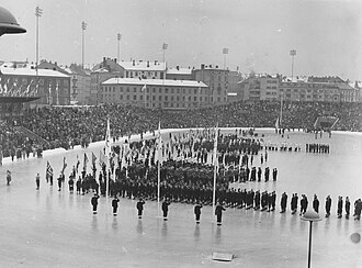 Long-shot of Olympic stadium with many athletes standing in neat formation behind their national flags